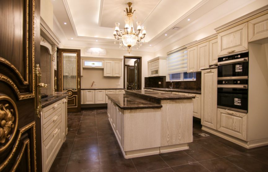 A spacious luxury kitchen in Kolkata, adorned with a chandelier and marble countertops, reflecting high-end interior design.